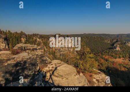 Rocks of the Elbe Sandstone Mountains in autumn with sunshine and blue sky. Rock formation in Saxon Switzerland with deciduous and coniferous trees Stock Photo