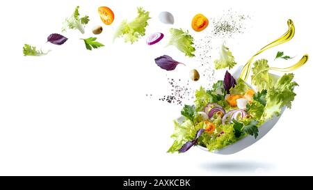 A white plate with salad and floating in the air ingredients: olives, lettuce, onion, tomato, ?ozzarella ?heese, parsley, basil and olive oil. Vegetar Stock Photo