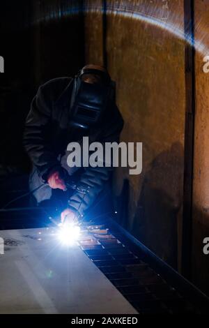 worker in protective uniform and mask welding metal. man using electric welding machine Stock Photo