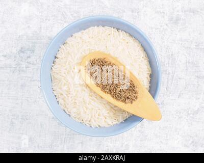 Indian long grain Basmati rice in blue ceramic bowl, cumin (jeera) on white concrete background Stock Photo