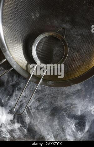 Stainless Steel Fine Mesh Strainer Colander Flour Sieve with Handle on dark background poudered with flour. Stock Photo