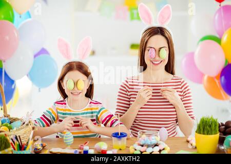 Close-up portrait of nice attractive funky creative cheerful girls small little pre-teen sister wearing bunny ears covering eyes with decorative eggs Stock Photo