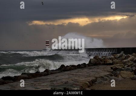 Dramatic stormy winter sunset at the Douro river mouth with big wave splash against north pier and beacon. Stock Photo