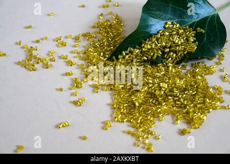 Yellow tubular toho beads and green ivy leaf on light cream background. Beads used for embelishing garments. Stock Photo