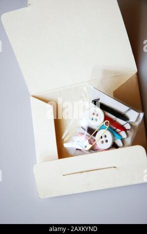 Sewing kit cardboard with buttons, needles and color thread on grey background vertical Stock Photo