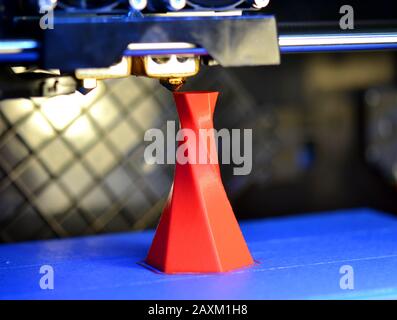 3D printer printing isolated volume triangular object red color on the basis of blue and black background close-up. Modern 3d printing technology Stock Photo