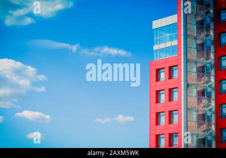 modern building with a red square windows and mirrored glass on the background of blue sky with clouds on a sunny day Stock Photo