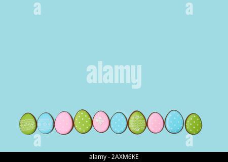 From above view of ginger glazed cookies isolated on blue background. Homemade lovely delicious pastry in shape of colorful eggs lying in row on table. Concept of spring and easter holidays. Stock Photo