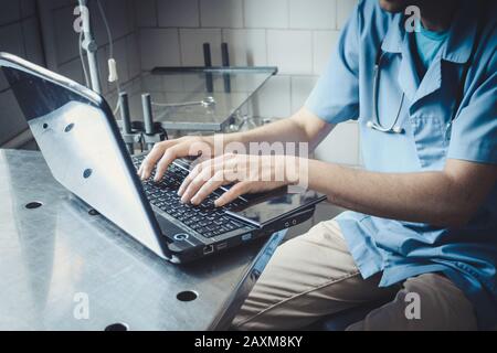 doctor in blue uniform sitting at the table and typing on laptop, filter Stock Photo