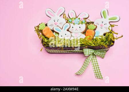 From above view of glazed cookies in shape of lovely bunnies and carrots lying in box with fake green grass, bow isolated on pink background. Spring and easter holidays concept. Stock Photo