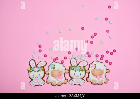 From above view of small colorful chocolate balls in crispy sugar shell isolated on pink background. Easter ginger glazed cookies in shape of bunnies in wreaths and sheep in row. Holidays concept. Stock Photo