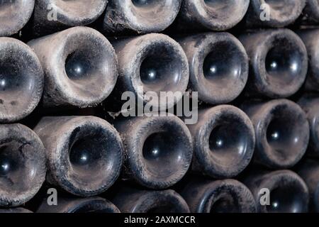 Closeup pattern from bottom of old dark dusty wine bottles in rows in cellar, basement, wine warehouse, winery. Concept vault with old rare wines, exc Stock Photo