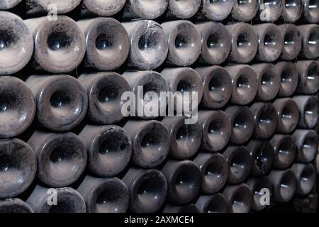 Closeup pattern from bottom of old dark dusty wine bottles in rows in cellar, basement, wine warehouse, winery. Concept vault with old rare wines, exc Stock Photo