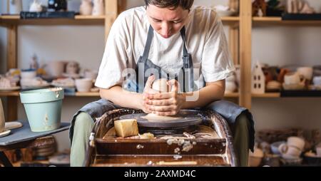 Potter working on a Potter's wheel making a vase. Young woman forming the clay with her hands creating jug in a workshop Stock Photo