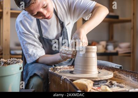 Potter working on a Potter's wheel making a vase. Young woman forming the clay with her hands creating jug in a workshop. Stock Photo