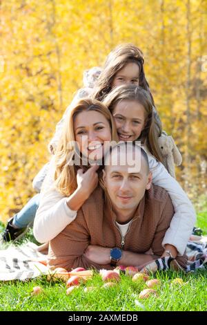Cheerful daughters hugging delighted parents while lying on grass during picnic on sunny autumn day in park Stock Photo