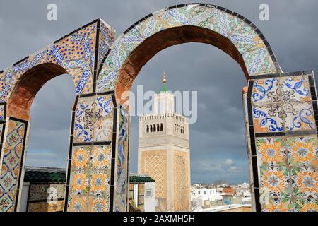 View on the minaret of Ez Zitouna Mosque (Great Mosque) through colorful tiled arches, located on a roof overlooking the medina of Tunis, Tunisia Stock Photo