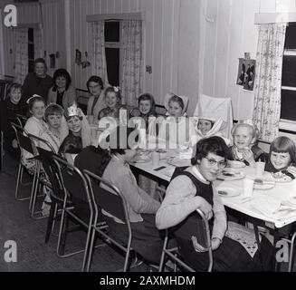 1960s, historical, young girl scouts, 'Brownies' some dressed in costumes, sitting together at a long table having a tea party in a village hall, England, UK. Originally known as 'Rosebuds', they were were renamed Brownies by the founder of the Scout movement, Lord Baden-Powell.  'Brownies' comes from the story 'The Brownies' by Juliana Horatia Ewing written in 1870. Stock Photo