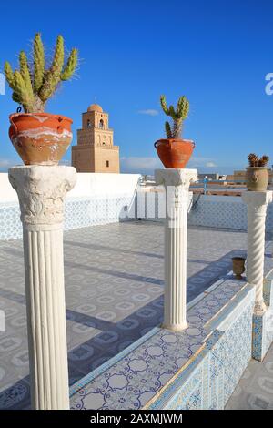The minaret of the Great Mosque of Kairouan, Tunisia, viewed from a tiled terrace, with cactus plants in the foreground Stock Photo