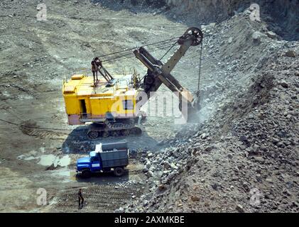 huge excavator, truck and man standing next on granite quarry, filter Stock Photo