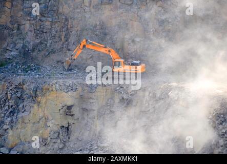 orange digger working in the granite quarry Stock Photo