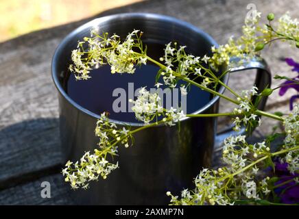 white flower in front of a metal cup on a wooden table Stock Photo