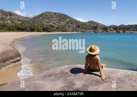 Curly hair man with hat and swimsuit, on top of rock, admiring the bay Stock Photo