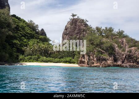 Isolated tropical small sandy beach, surrounded by palm trees and rock Stock Photo