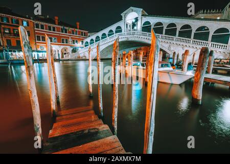 Venice, Italy. A night-time view of pier at iconic Rialto Bridge, spanning over the Grand Canal lit by city illumination