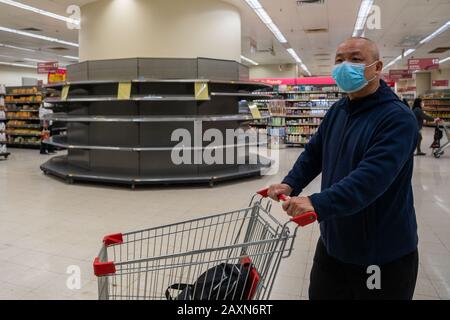 A shopper wearing a protective facemask walks past empty supermarket shelves, usually stocked with toilet paper and kitchen rolls.Panic grows in Hong Kong as the city  has confirmed the 50th case of Novel coronavirus (2019-nCoV). Over 40,000 cases of the virus has confirmed around the world, it has so far claimed over 1000 lives. Stock Photo