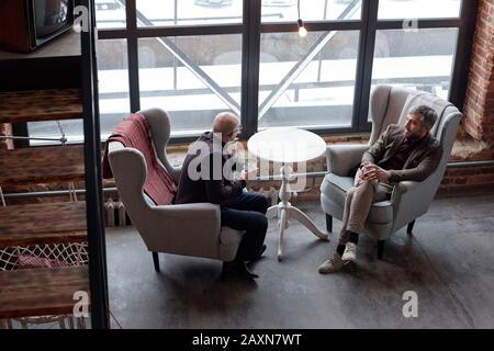 Above view of stylish middle-aged businessmen sitting in comfortable armchairs and drinking alcohol in lobby bar Stock Photo