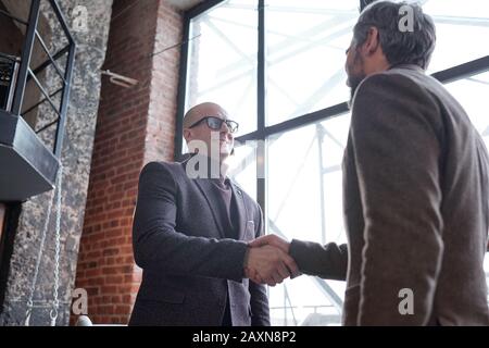 Below view of bald man in eyeglasses making handshake with business partner while meeting him in lobby Stock Photo