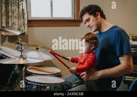 Father teaching baby boy to play drums. Parent with toddler child having fun and spending time together. Dad and kid playing music. Family hobby activ Stock Photo