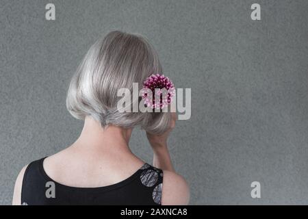 Gray-haired lady with red dahlia flower, on neutral background with copy space.
