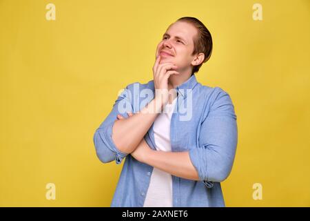 A man in a blue shirt on a yellow background smiles and thought about the pleasant. Close up. Stock Photo