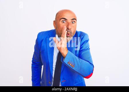 Middle age businessman wearing suit standing over isolated white background hand on mouth telling secret rumor, whispering malicious talk conversation Stock Photo