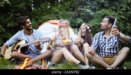 Group of friends camping and sitting around camp fire Stock Photo