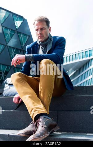 Businessman sits in front of modern office buildings, Frankfurt on the Main, Hessen, Germany Stock Photo