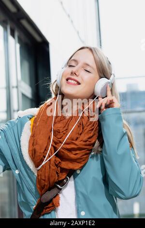 Young woman hears pious music with earphones in front of office building, portrait Stock Photo