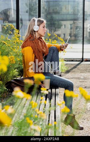 Young woman sits in front of office building and hears music Stock Photo