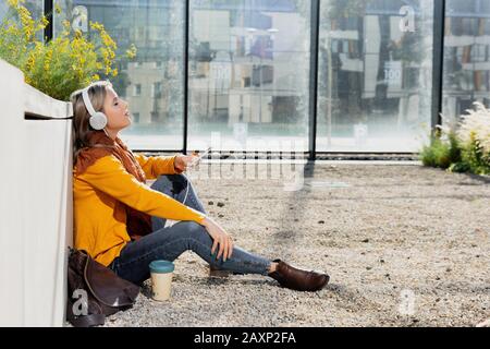 Young woman sits in the floor in front of office building and hears music Stock Photo