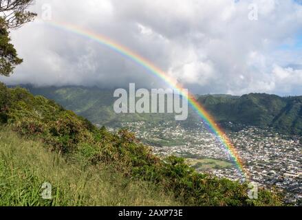 Bright rainbow over the suburbs of Woodlawn and Manoa in a valley above Honolulu on Hawaii Stock Photo