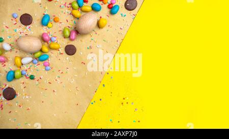 Wooden Easter eggs, sweets on yellow background, copy space Stock Photo