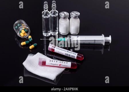 Blood test tube with the Coronavirus disease for virus test and research. Blood test tube with ampoules, syringe and medicine on black desk Stock Photo