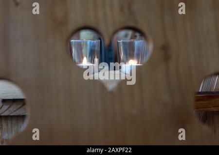 Valentine's day heart shaped frame, peephole in wooden chair, candle glass in background, closeup. Stock Photo