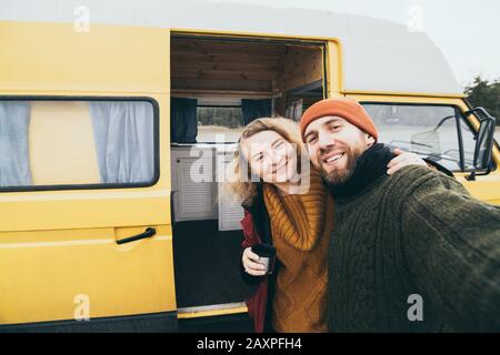 Young happy couple taking selfie in front of their yellow camper van Stock Photo