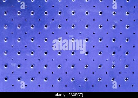 Close-up of a blue metallic surface filled with round holes that create a reticular geometric texture Stock Photo