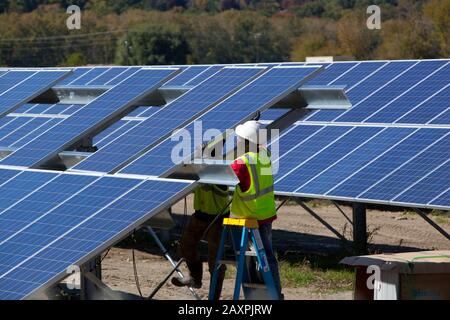 Workmen installing an array of solar panels in an open field in southern Vermont Stock Photo