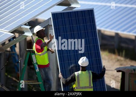Workmen installing an array of solar panels in an open field in southern Vermont Stock Photo