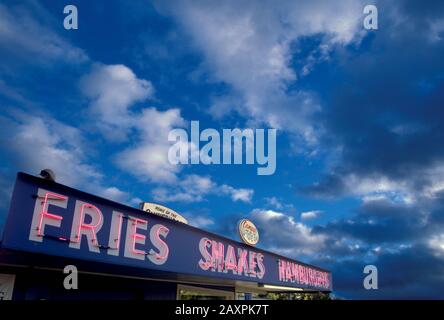 Neon sign on a diner advertising fries shakes and hamburgers under a darkening evening sky Stock Photo